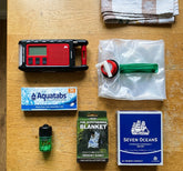 Three-Day Basics Kit with Radio laid out on a kitchen table: Midland ER300 Pro radio, jerry can, water tablets, matches, foil blanket and Seven Oceans ration block